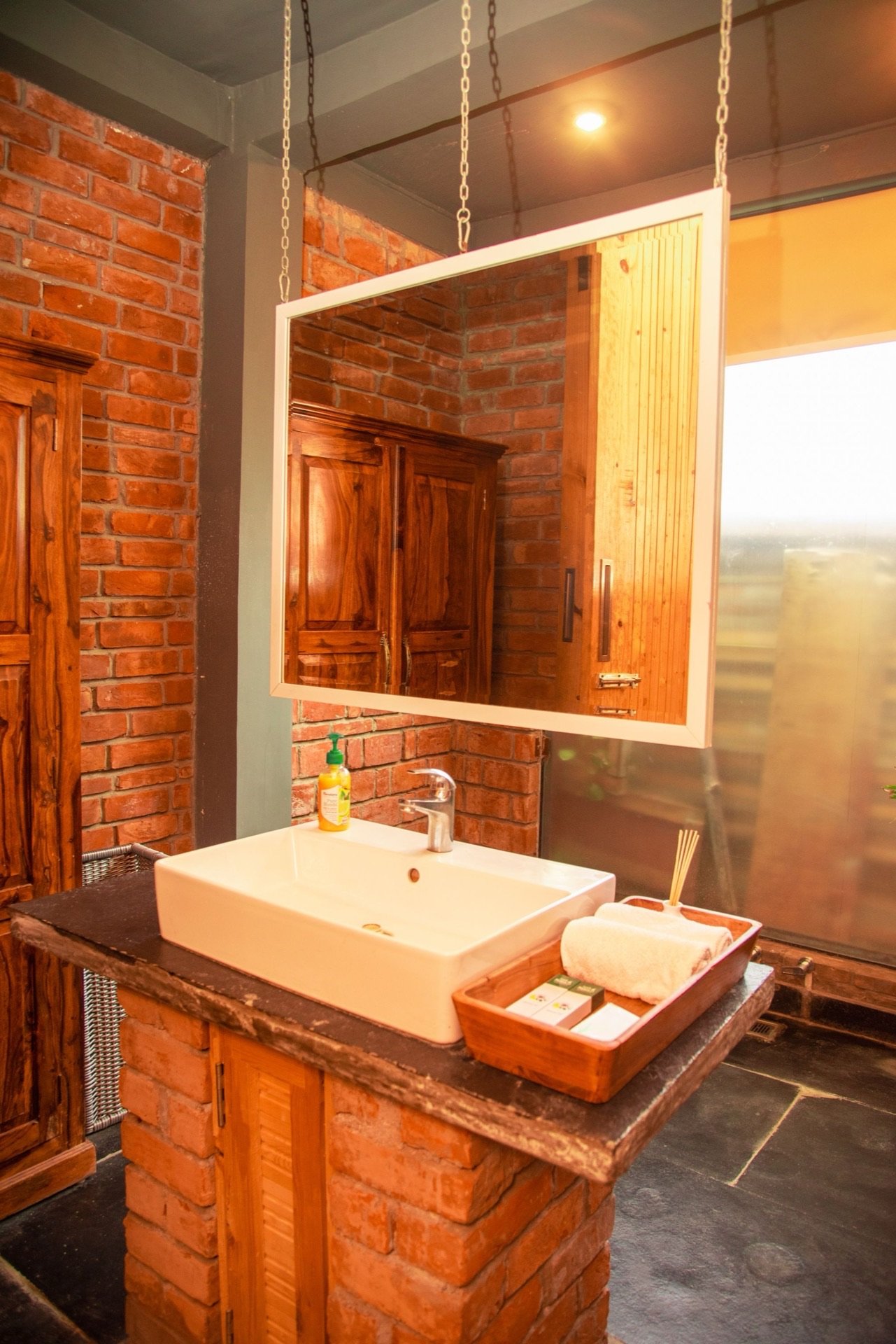Luxury en-suite bathroom with chain-hung mirror and brick wall — We Woods Farm Gurgaon