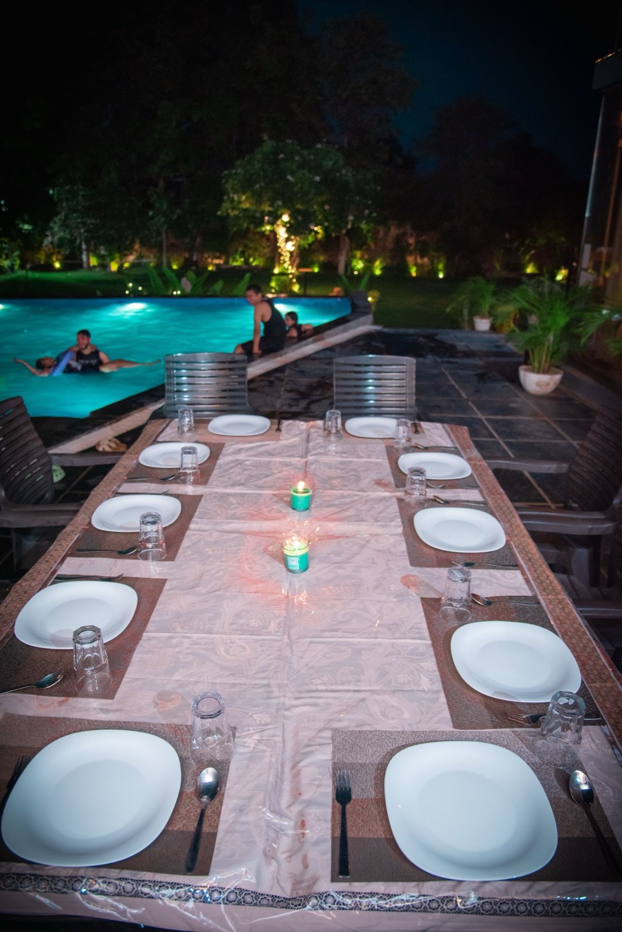 Night view of chemical-free infinity pool with candlelit dining — We Woods Farm, farmhouse with pool in Gurgaon Manesar